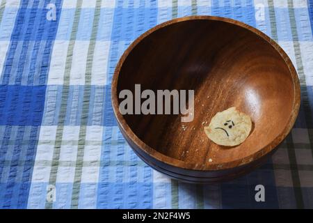 Una faccia triste sull'ultimo chip di patate in una ciotola di legno marrone, a destra della cornice, con illuminazione laterale e ombre Moody per contribuire a creare un senso di solitudine Foto Stock