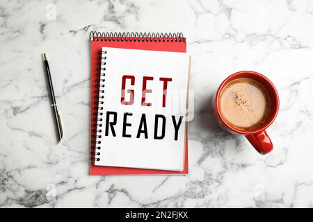 Notebook con testo Get Ready, tazza di caffè e penna su marmo bianco, piatto Foto Stock