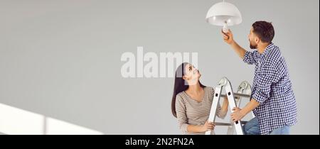 Banner con felice giovane famiglia coppia che cambia lampadina a risparmio energetico insieme Foto Stock