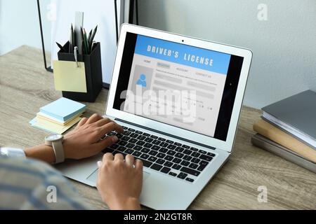 Donna che utilizza il computer portatile per compilare il modulo di domanda di patente di guida al tavolo in ufficio, in primo piano Foto Stock