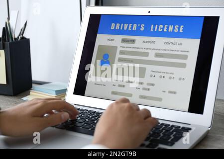 Donna che utilizza il computer portatile per compilare il modulo di domanda di patente di guida al tavolo in ufficio, in primo piano Foto Stock