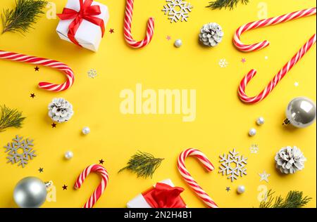 Cornice di canne caramelle e decorazioni natalizie su sfondo giallo, piatto. Spazio per il testo Foto Stock