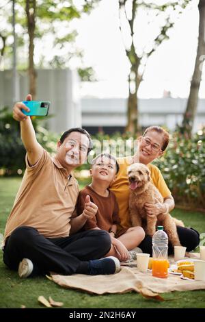 Uomo anziano sorridente che prende selfie con sua moglie, nipote e cane Foto Stock