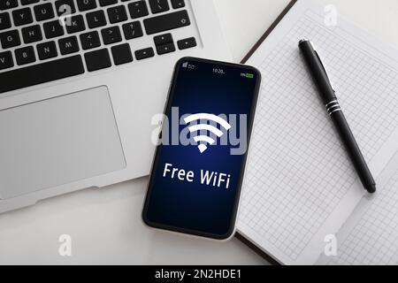 Smartphone collegato al WiFi sul tavolo con computer portatile e blocco note sul tavolo, piatto Foto Stock