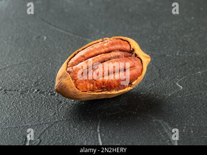 Primo piano delle noci pecan in-shell incrinate su fondo di cemento scuro Foto Stock