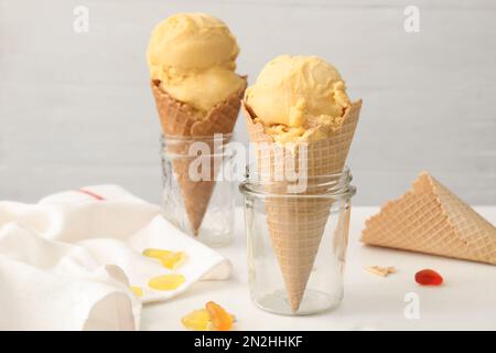 Delizioso gelato giallo in cialda di wafer e caramelle di gelatina su tavolo bianco Foto Stock