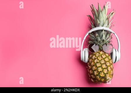 Vista dall'alto di ananas con cuffie e occhiali da sole su sfondo rosa, spazio per il testo. Concetto creativo Foto Stock