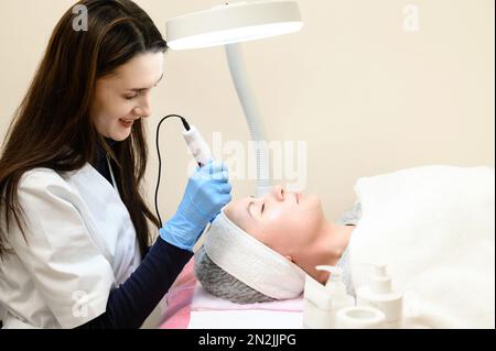 Un cosmetologo esegue una procedura di ringiovanimento mesoterapico con l'aiuto di dermapen, una visita ad un cosmetologo. Foto Stock