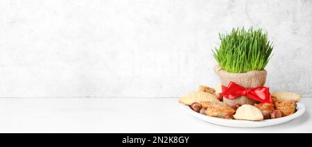 Erba di grano verde con dolci per Novruz Bayram su sfondo chiaro con spazio per il testo. Foto Stock