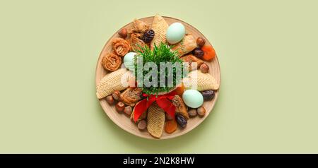 Piatto con dolci, uova e erba di grano su fondo verde. Novruz Bayram celebrazione Foto Stock