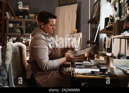 una ragazza artista in studio inserisce un'immagine in una cornice Foto Stock