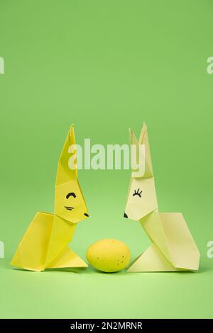 Origami di Pasqua - due coniglietti di carta e un uovo, sfondo verde. Artigianato per le vacanze, fatelo da soli Foto Stock