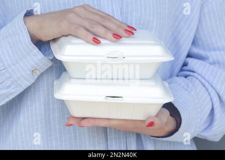 Mani di donna che tengono scatole da pranzo in schiuma da asporto. Contenitori per alimenti monouso, primo piano. Foto Stock