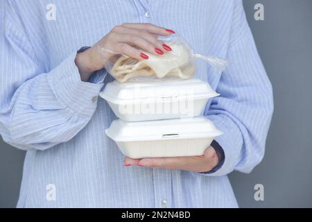 Mani di donna che tengono scatole da pranzo in schiuma da asporto. Contenitori per alimenti monouso, primo piano. Foto Stock