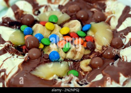 Miscela di cioccolato con biscotti e diversi tipi di pezzi di cioccolato e crema con ananas fresco e pezzi di banane sulla parte superiore su una torta di pasta Foto Stock