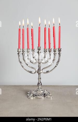 Menorah d'argento con candele accese sul tavolo su sfondo grigio chiaro. Hanukkah celebrazione Foto Stock