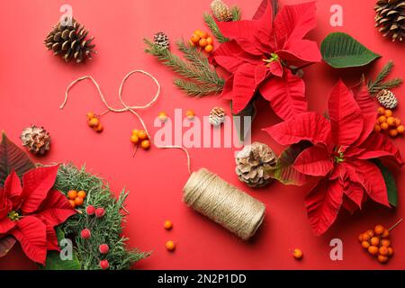 Composizione piatta con poinsettie (fiori di Natale tradizionali) e decorazioni su sfondo rosso Foto Stock