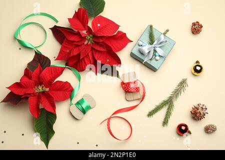 Composizione piatta con poinsettie (fiori di Natale tradizionali) e decorazioni per le vacanze su sfondo beige Foto Stock