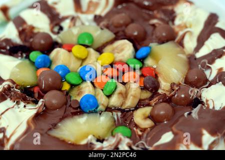 Miscela di cioccolato con biscotti e diversi tipi di pezzi di cioccolato e crema con ananas fresco e pezzi di banane sulla parte superiore su una torta di pasta Foto Stock