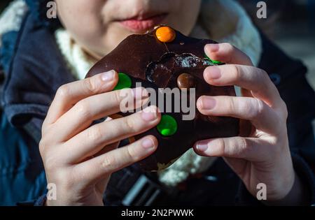 Primo piano di un ragazzo che mangia una ciambella al cioccolato con farcitura dolciaria Foto Stock