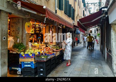 Un'elegante donna addetta allo shopping in un negozio di alimentari a Salizada San Canzian nel sestiere di Cannaregio in estate, Venezia, Veneto, Italia Foto Stock