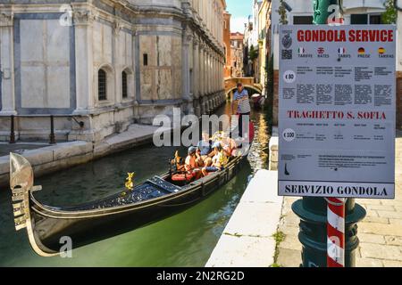 Gondola con i turisti sul canale Rio dei Miracoli e un cartello con le tariffe ufficiali delle gite in gondola in primo piano, Venezia, Veneto, Italia Foto Stock