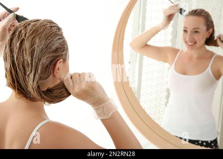 Giovane donna che applica la tintura sui capelli vicino specchio all'interno Foto Stock