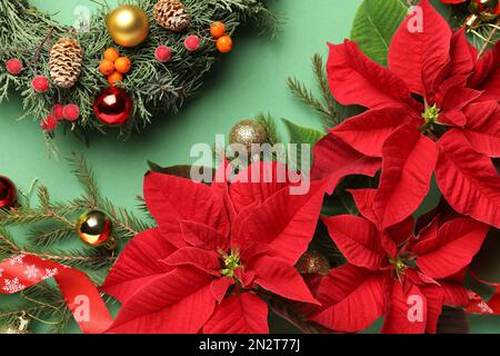 Composizione piatta con poinsettie (fiori di Natale tradizionali) e decorazioni per le vacanze su sfondo verde Foto Stock