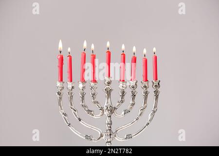 Menorah d'argento con candele accese su sfondo grigio chiaro. Hanukkah celebrazione Foto Stock