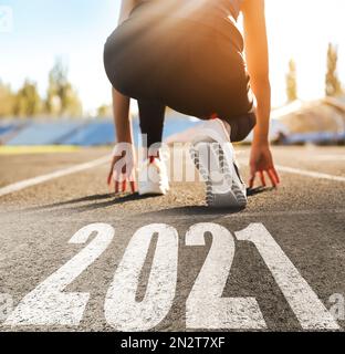 Inizia il nuovo anno con nuove idee e idee. Donna sportiva pronta per correre vicino a 2021 numeri su strada, primo piano Foto Stock