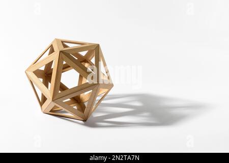 Forma platonica solida di icosaedro in legno chiaro che getta l'ombra su sfondo grigio Foto Stock