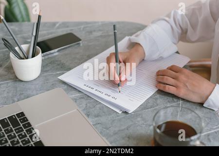 Primo piano di una donna seduta alla scrivania che scrive una lista da fare Foto Stock