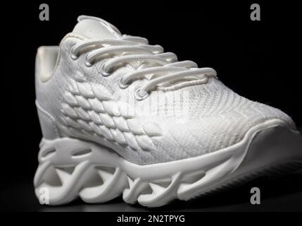 Sneaker in tessuto bianco con suola in rilievo su sfondo nero. Foto Stock