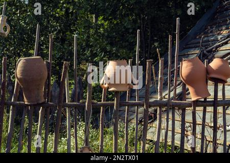 Vecchie pentole di argilla appese capovolte su recinzione di legno. Vasi antichi fatti a mano asciutti all'aperto su colonne. Articoli per la casa rurale, stoviglie. Vita di campagna Foto Stock