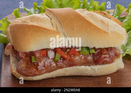 Primo piano di un choripan, tipico panino argentino con chorizo e salsa creola su un asse di legno. Foto Stock