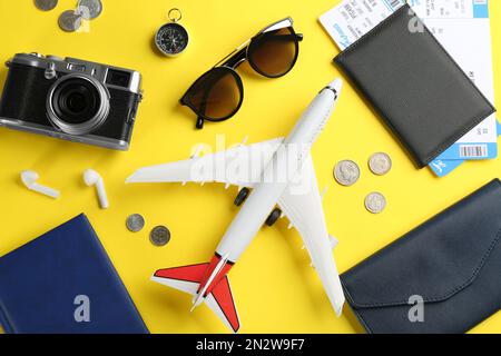 Composizione piatta con velivolo giocattolo e oggetti da viaggio su sfondo giallo Foto Stock