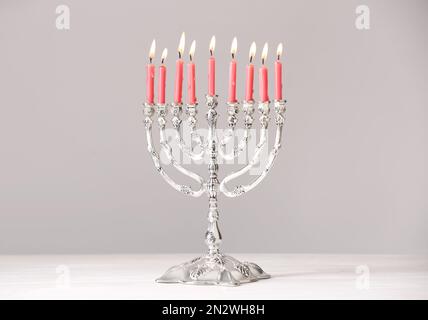 Menorah d'argento con candele accese sul tavolo su sfondo grigio chiaro. Hanukkah celebrazione Foto Stock