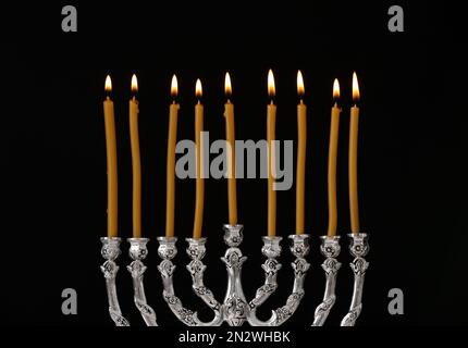 Menorah d'argento con candele accese su sfondo nero. Hanukkah celebrazione Foto Stock