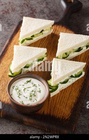 Panini inglesi con cetriolo fresco, aneto e formaggio cremoso primo piano su un asse di legno sul tavolo. Verticale Foto Stock