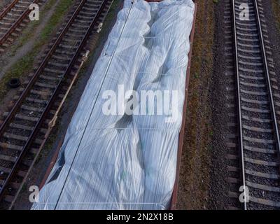 Vista dall'alto su un vagone ferroviario senza tetto carico di enormi sacchi bianchi e in attesa alla stazione nella città di Kyiv, Ucraina. Foto Stock