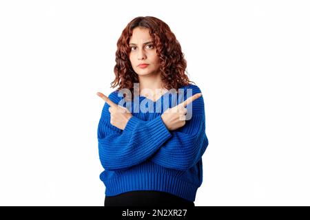 Giovane donna caucasica che indossa pullover maglione in piedi isolato su sfondo bianco incrocia braccia e punti laterali, sceglie tra due opzioni. Foto Stock