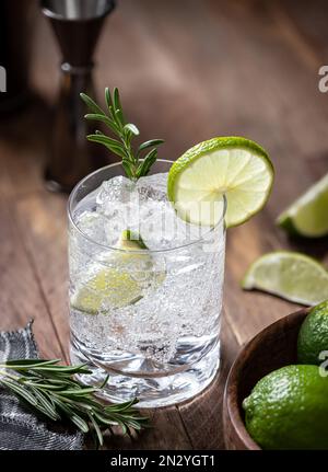 Cocktail tonico e gin con fettine di lime, rosmarino e ghiaccio su un tavolo rustico in legno. Angolo di visualizzazione elevato e spazio di copia Foto Stock