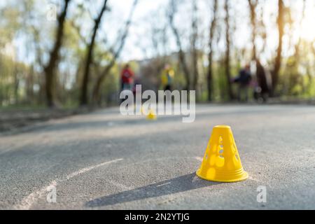 Un gruppo di bambini si diverte imparando la slalom dello skate a rotelle in linea con coni di plastica su strada nel parco cittadino all'aperto nella soleggiata giornata primaverile Foto Stock