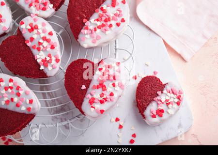 Biscotti rossi di velluto o brownie a forma di cuore in glassa di cioccolato su uno sfondo rosa romantico. Dessert per San Valentino, la mamma o la donna Foto Stock