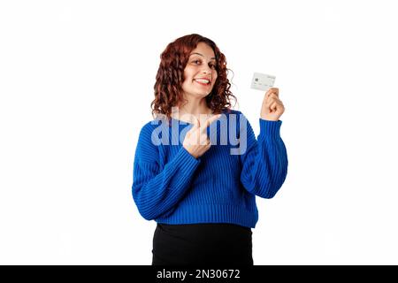 Ritratto di donna in piedi isolato su sfondo bianco tiene una carta di credito in mano e punta alla carta di debito con il dito indice. Molto felice e di nuovo Foto Stock