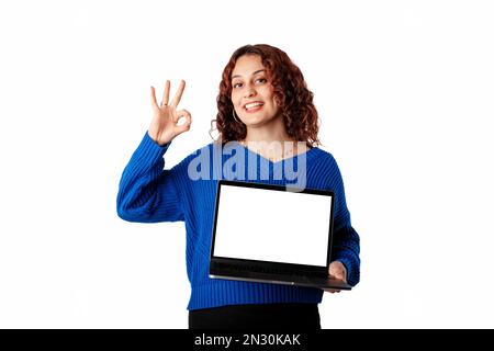 Ritratto di donna che indossa un maglione a maglia blu isolato su sfondo bianco tenendo un notebook con uno schermo bianco mockup, sorride a th Foto Stock