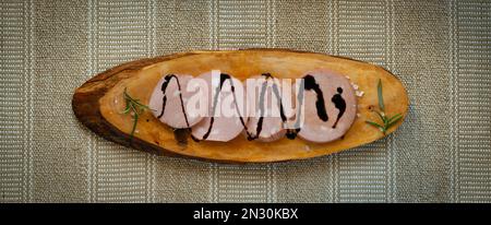 Fettine di mortadella IGP bolognese su un tagliere di legno rustico con uno smalto all'aceto balsamico modenese Foto Stock