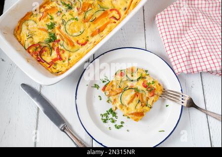 Frittata con verdure mediterranee come pomodori, carote, zucchine, cipolle, peperoni ed erbe aromatiche in un piatto da forno su fondo bianco. Foto Stock