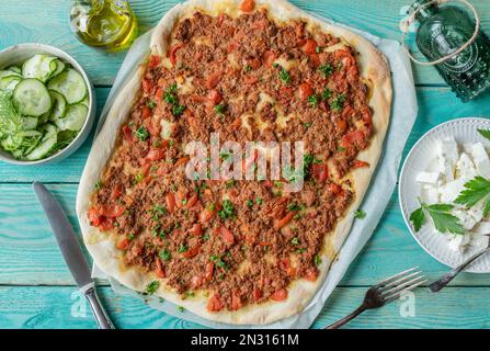 Pizza turca o lahmacun con macinato di manzo, verdure. Servito con feta e insalata di cetrioli su sfondo turchese. Giacitura piatta Foto Stock