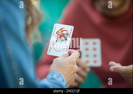 Carte da gioco nel giardino primaverile. Una donna gioca a carte e tiene in mano un joker. Foto Stock